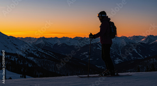 Skier carving a snowy ridge at sunset with mountain silhouettes