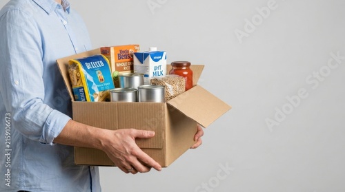 Young professional holding cardboard box filled with assorted food donations for charity drive