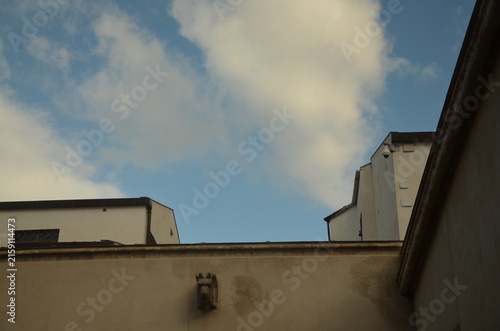 Принти на полотні Low angle view of historic stone and plaster building facades featuring a small sculpted stone corbel and a modern security camera against a blue sky with clouds in Sicily, Italy
