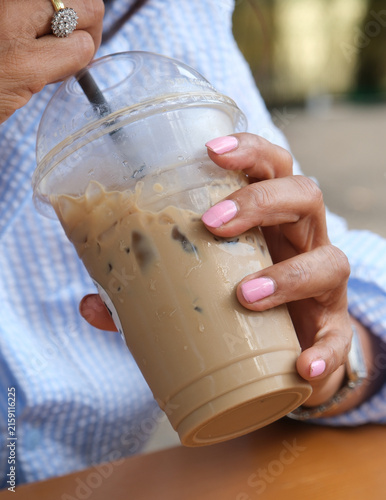 Bild auf Leinwand Kalter Kaffee mit Eis im Becher in der Hand von einer Frau mit pinkfarbig lackie