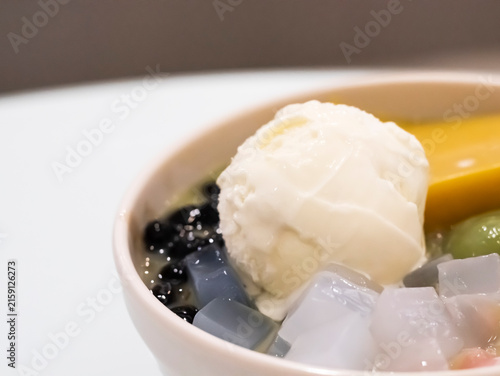 Macro shot focusing on a scoop of creamy vanilla ice cream resting in a bowl of Asian dessert, surrounded by tapioca pearls, jelly cubes, pudding, and mochi.