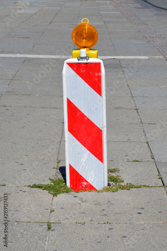 Photography A temporary plastic traffic marker post with an amber flashing light stands on a paved sidewalk to signal a construction zone