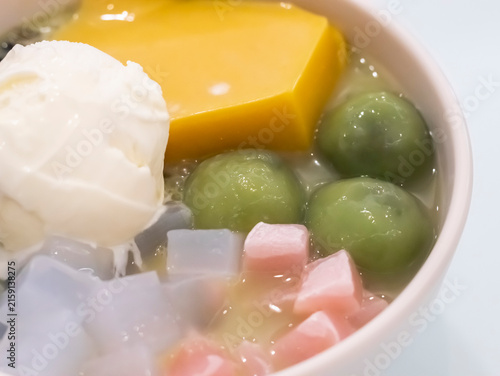 Close-up shot of an Asian dessert bowl highlighting a scoop of vanilla ice cream, yellow pudding, green mochi balls, and colorful jelly cubes in a sweet milky base.