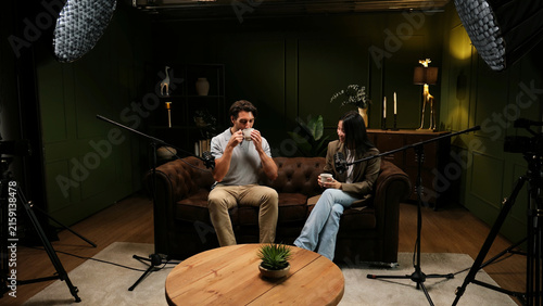 Obraz na płótnie Two people sitting on a couch and holding mugs while recording a podcast episode