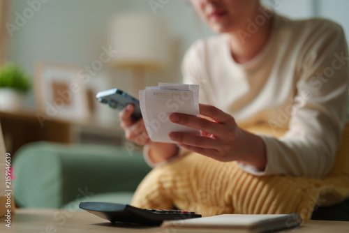 фотографія Person reviewing multiple receipts with smartphone and calculator at home, expen