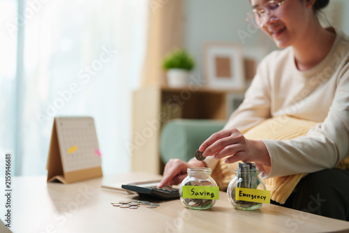 Canvastavla Woman putting coin into saving jar beside emergency fund jar while budgeting at