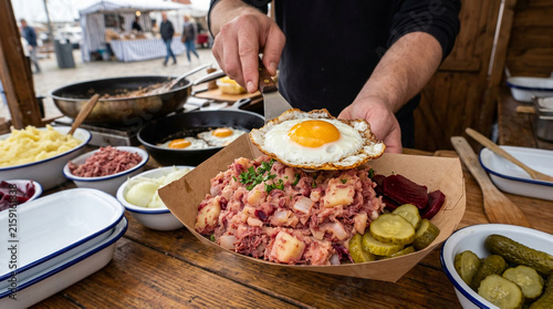 Chef preparing a gourmet breakfast platter with fried egg and potato hash at an outdoor food market