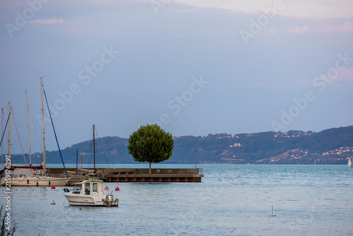 Konstfotografi Paysage paisible du lac de Neuchâtel avec un petit voilier amarré, une jetée et les collines du littoral en arrière-plan