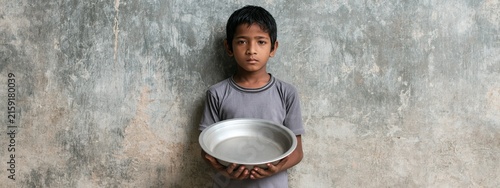Underprivileged Boy Holding Empty Bowl Against Worn Concrete Wall