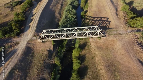 Wide aerial shot of a long iron truss railway bridge spanning a wide river in a lush green countryside. Landscape structure crossing water nature 
