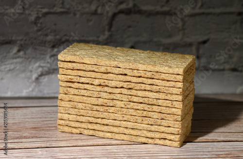 Canvastavla Stack of rectangular crispbread on a wooden surface against a dark brick wall