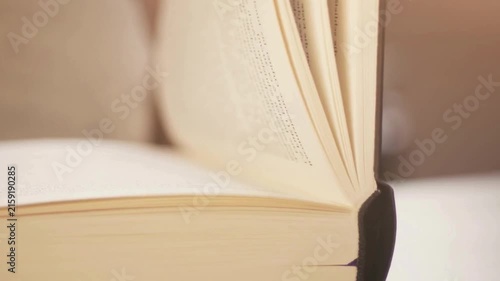 Person closing thick hardcover book with pages fluttering as fingers touch paper edges in slow motion cinematic closeup footage of reading relaxing pastime.