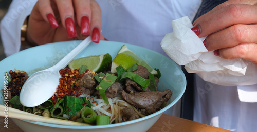 Cuadro en lienzo Nahaufnahme von Frauenhänden mit rot lackierten Fingernägeln, die einen Löffel über eine Schüssel thailändischer Nudelsuppe halten