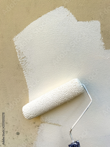 Close up view of smooth white masonry paint being applied to an exterior wall using a paint roller.