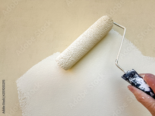 Close up view of smooth white masonry paint being applied to an exterior wall using a paint roller.
