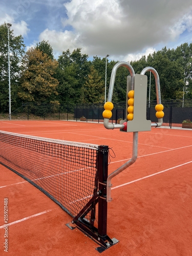Canvastavla A tennis scoreboard stands near the net in the foreground, with gravel courts stretching behind, ready for match play and spectator updates