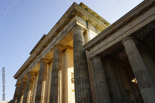 Golden morning light falls through the historic columns of the landmark Brandenburger Tor, Berlin, Germany, during sunrise or dawn. 
