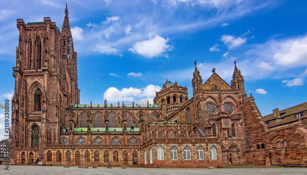 Fototapeta premium Wide view of Strasbourg Cathedral showing its Gothic facade, monumental tower, ornate tracery, stained glass windows, sandstone walls and green copper roofs in Strasbourg, France.
