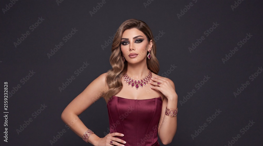 Fototapeta premium Stunning woman wearing rose gold ruby red rhombus jewelry set in burgundy satin corset dress, model portrait with copy space