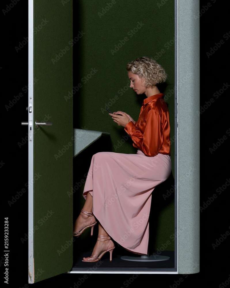 Obraz premium Woman in a satin shirt and long skirt using a smartphone inside a soft felt acoustic phone booth, for hybrid workplace and office design campaigns