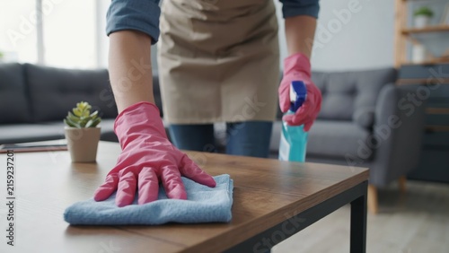 Person cleaning wooden table with spray and cloth in living room