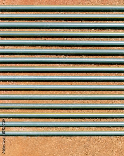 Galvanized pipework in parallel rows, featuring oxidized weld beads and metallic spangle on compacted soil for industrial design patterns