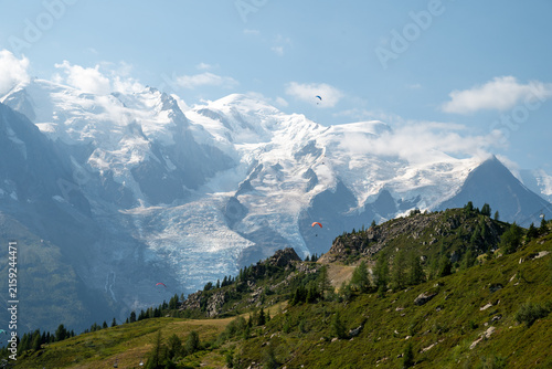 Dramatic summer view of Mont Blanc massif, glaciers, green alpine slopes and paragliders near Chamonix, France.