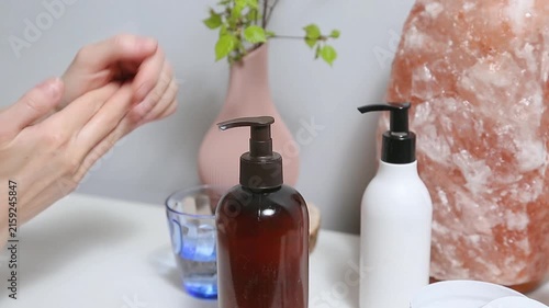 Woman performing a relaxing hand and wrist self massage as part of a wellness and self care routine at home. Female applying cream from product bottle to care moisturizing her palms skin