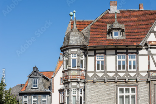 Traditional half-timbered building in Goslar, Germany, featuring a detailed historic wooden bay window, slate facade elements, red tiled roof, and fine decorative carvings against a clear blue sky.