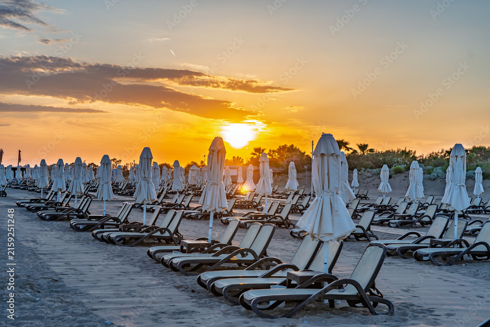 Naklejka premium Mediterranean sunset with long rows of sun loungers and beach umbrellas in Antalya, Turkey.