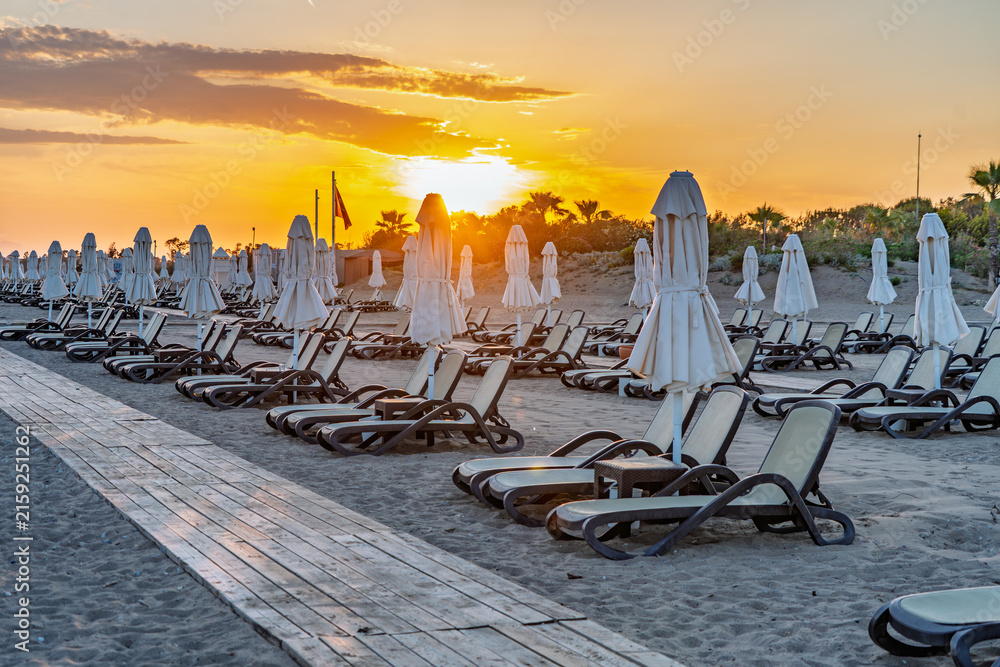 Fototapeta premium Backlit beach chairs and umbrellas beneath a glowing Mediterranean sunset in Antalya, Turkey.