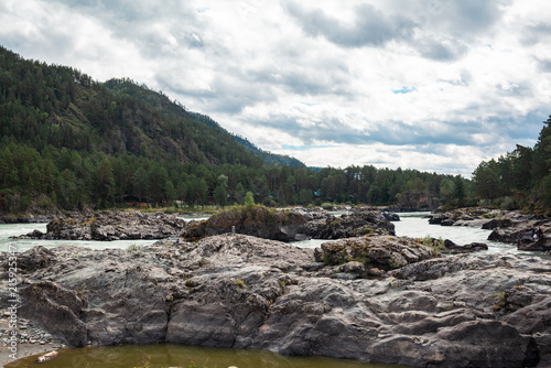 Obraz na plátně Rocky river scene features flowing water, with large boulders and lush green tre
