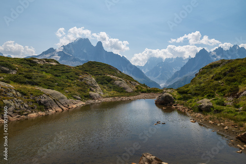Still alpine pond reflects rugged mountain peaks and summer clouds near Chamonix, France.