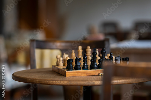 The game has begun, but the next move remains hidden - black and white pieces face each other. Vintage wooden chessboard with black and white chess pieces arranged for a strategic game on a table. 