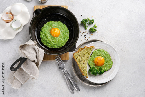 Healthy breakfast with fried eggs in broccoli puree, skillet and plate. Horizontal top view.