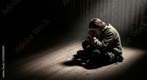 Person in green coat praying on wooden floor, symbolizing contemplation, hope, or despair in dramatic lighting.