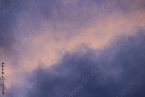 Soft pink twilight clouds diagonal band contrasting against moody dark purple storm clouds. Atmospheric cloudscape sky background perfect for artistic overlays, wallpapers, and creative design work.