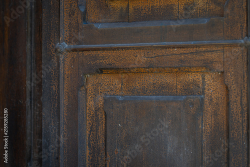 Close-up of an antique wooden door with weathered dark brown wood, rustic geometric panels, aged texture and natural patina, creating a timeless architectural background. 