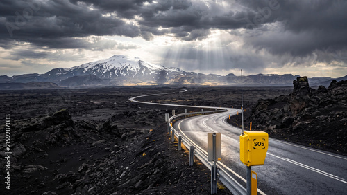 Windy road curving through a dark volcanic landscape under stormy skies