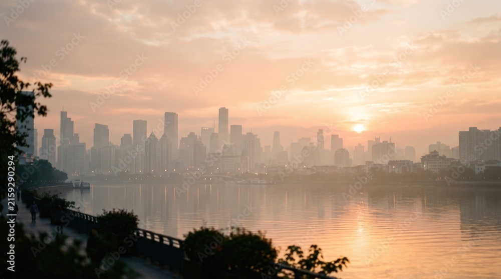 Fototapeta premium Modern City Skyline Reflected in Calm Waterfront During Warm Hazy Sunset