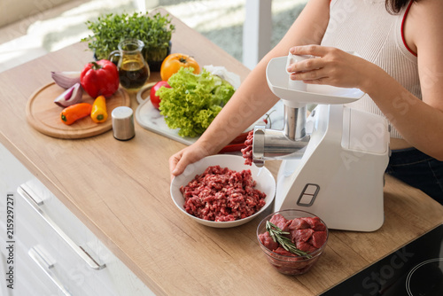 Fotografía Young woman using modern meat grinder in kitchen
