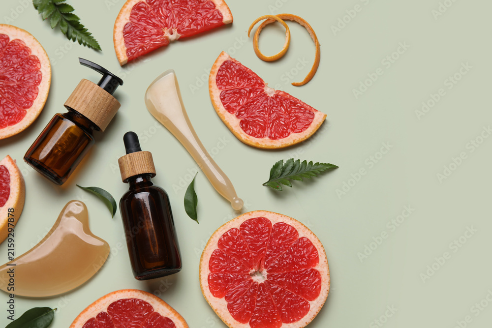 Fototapeta premium Composition with bottles of cosmetic products, facial massage tools and slices of grapefruit on green background, closeup