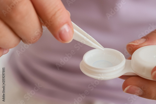 Quadro su tela Young woman with tweezers taking contact lens from container at home, closeup