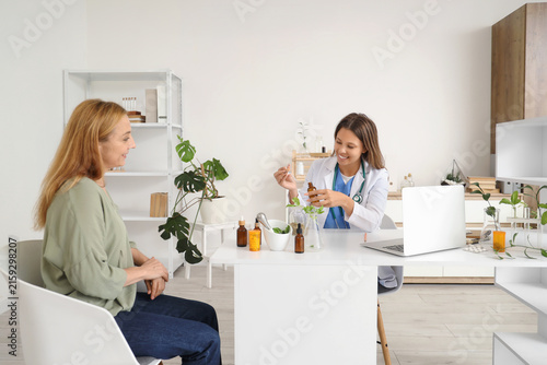 Obraz na płótnie Female homeopathic doctor with dropper bottle and mature woman at table in offic
