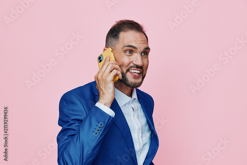 Photography A professional man in a blue suit on an isolated pink background, speaking on a yellow phone, displaying confident posture and dynamic emotion suitable for business use