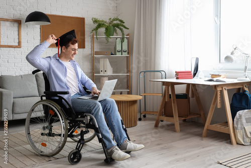 Male graduate in wheelchair with laptop video chatting at home