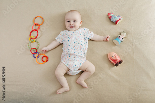 Cute 7 month baby boy lying among various playful colorful toys on beige blanket. Infant surrounded by vivid objects participating actively in sensory exploration and learning. 