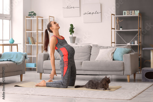 Sporty pregnant woman with cute cat doing yoga on mat at home