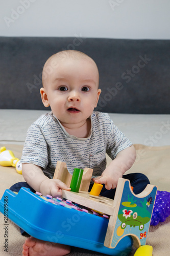 Cute 11 month baby boy among various playful colorful toys on beige blanket. Infant surrounded by vivid objects participating actively in sensory exploration and learning. 