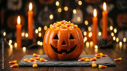 Halloween pumpkin candy bowl filled with candy corn on stone slate with candlelight background template